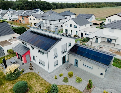 Luftaufnahme eines Wohngebiets mit Photovoltaikanlagen auf mehreren Hausdächern.
